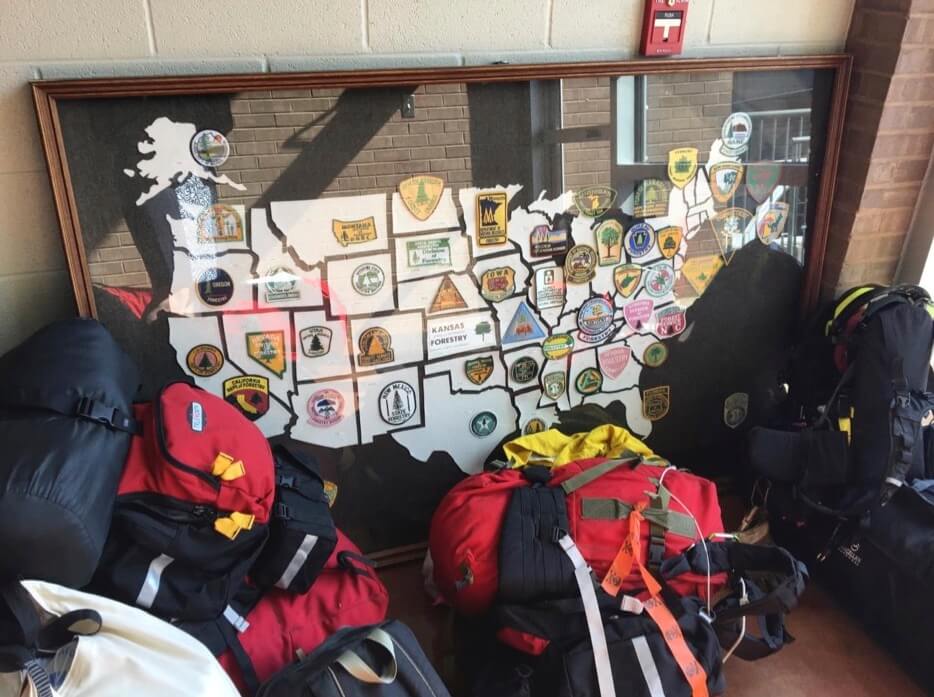 Packed duffel bags sit in front of a framed map of the United States. Each state on the map has the insignia of each state's respective Forestry Commission