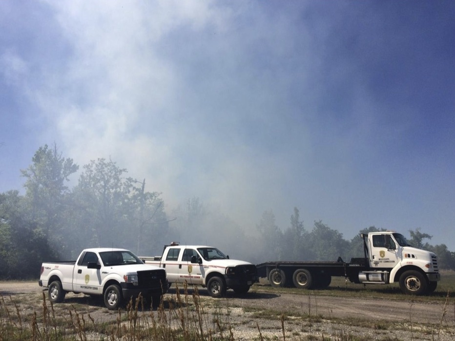 Three white trucks in a field, with fire smoke covering most of the photo