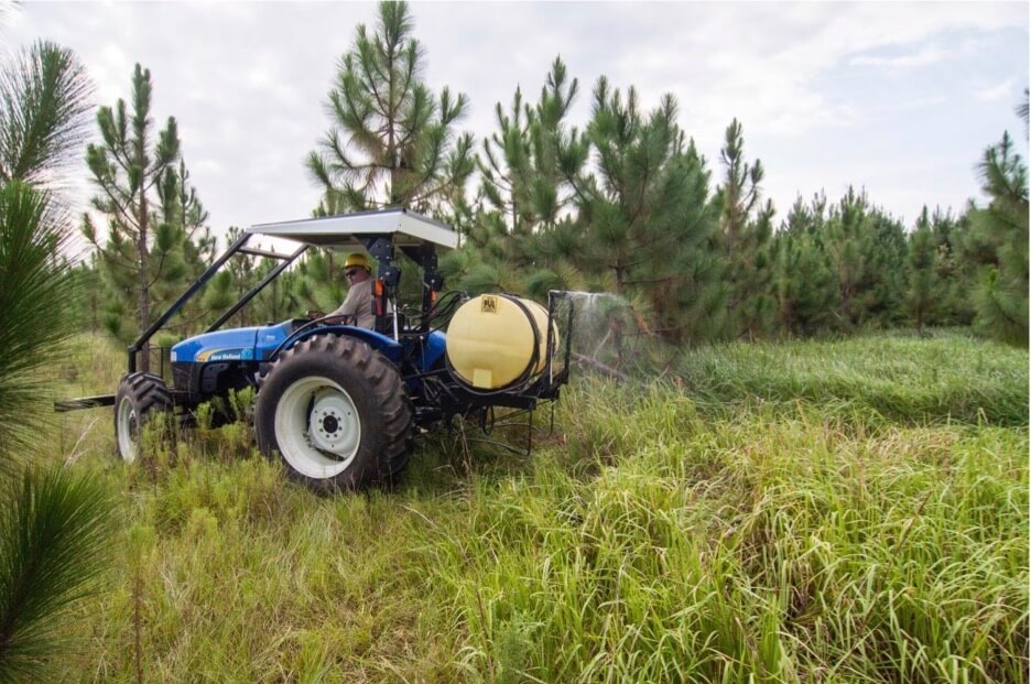 A small tractor driving through tall grass spraying pesticide