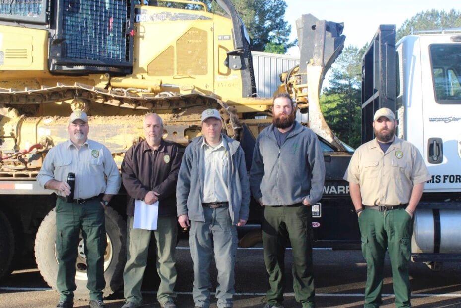 Five men standing in front of a bulldozer loaded onto a trailer truck