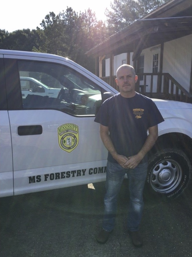 A man standing in front of a white truck with the MS Forestry Commission logo on the door.