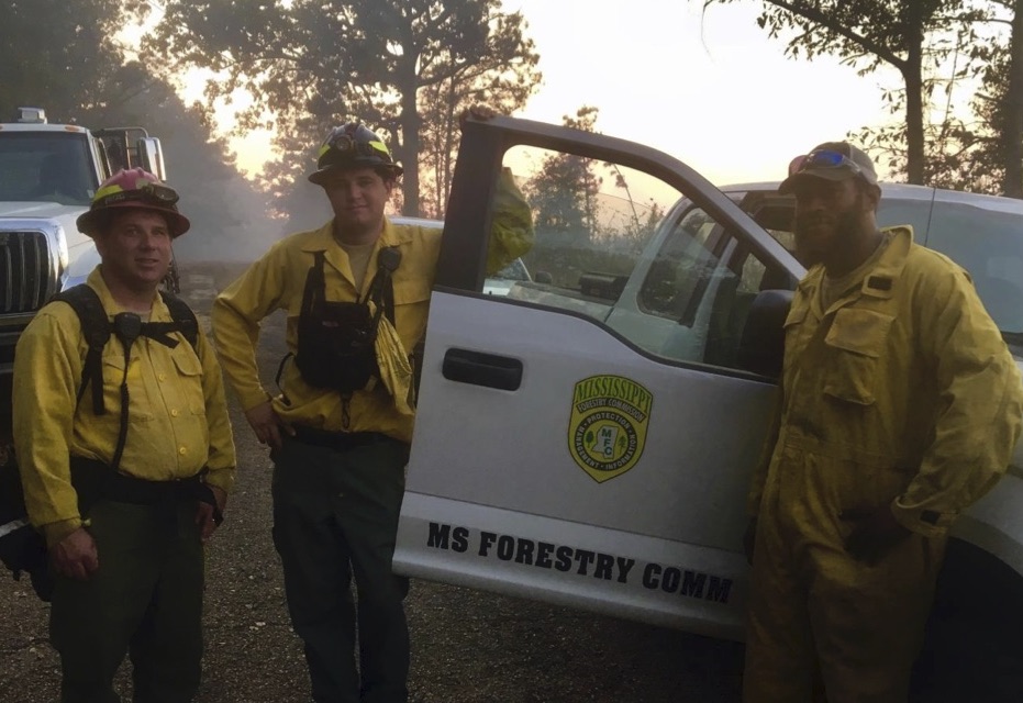 Three men standing in yellow clothes by an open truck door